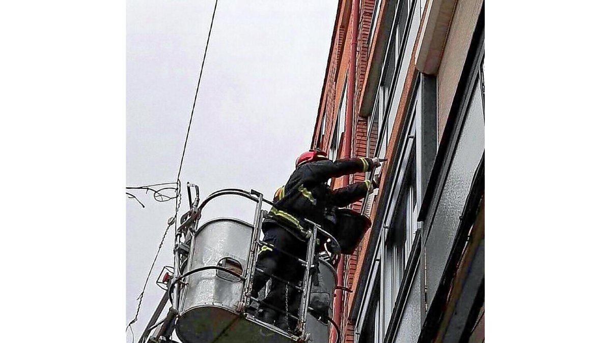 Varios bomberos se acercan a una fachada para ayudar con la borrasca.-E. M.