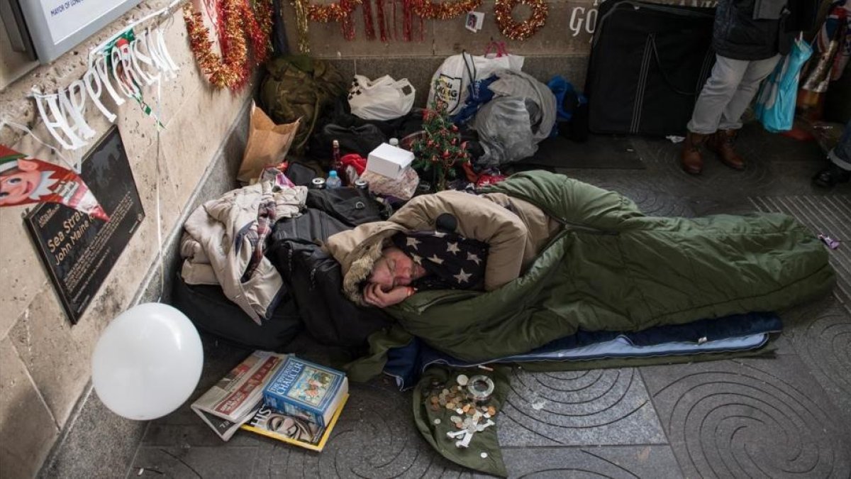 Un sintecho rodeado de motivos navideños que él mismo y un amigo colocaron en el exterior de la estación de metro de Green Park, el 16 de diciembre, en Londres.-/ GETTY IMAGES / CHRIS J. RATCLIFFE