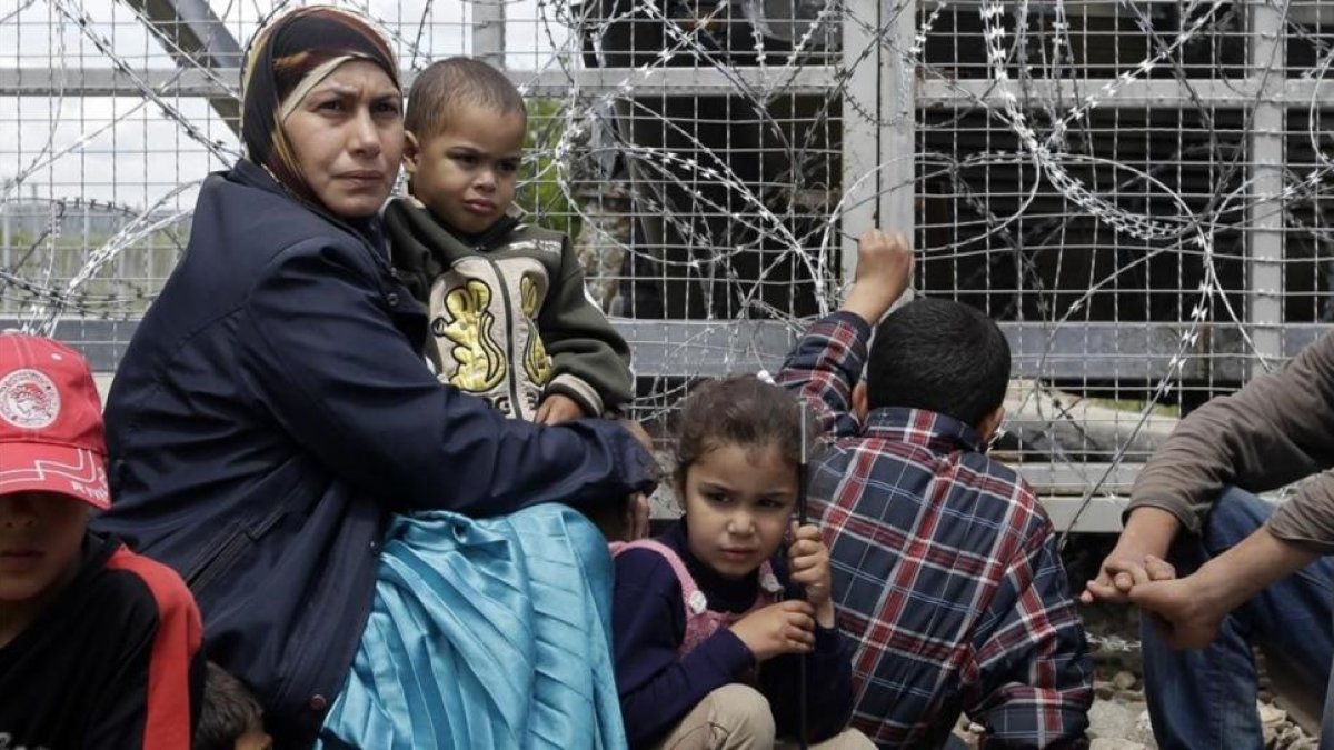 Un mujer migrante rodeada de niños, sentados junto a una valla durante una protesta por las penosas condiciones del campo de refugiados y contra el cierre del paso fronterizo de Idomeni (Grecia), este jueves.-AP / GREGORIO BORGIA
