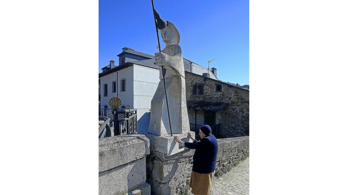 Una mujer toca la estatua de un peregrino del Camino de Santiago que hace de parada para los caminantes  en el pueblo leonés de Villafranca del Bierzo.-EL MUNDO