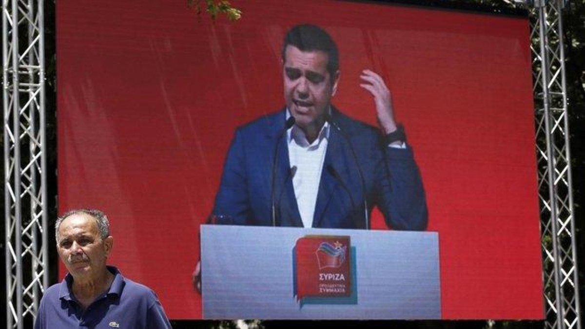 Un hombre pasa frente a una pantalla en la que se proyecta un mitin de Tsipras en Atenas, el pasado 18 de mayo.-YANNIS KOLESIDIS (EFE)