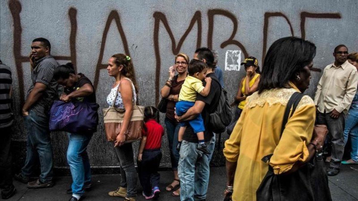 Venezolanos hacen cola frente a una pintada con la palabra hambre, en Caracas.-JUAN BARRETO (AFP)