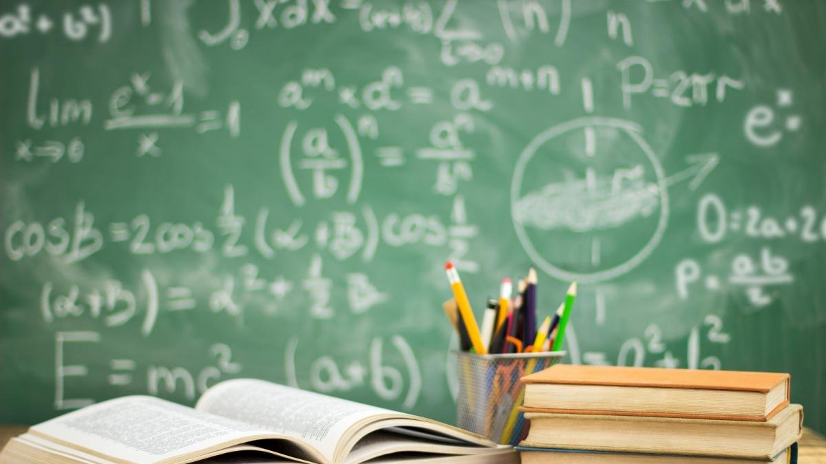 Libros y lápices con pizarra escrita con tiza de fondo.-EL MUNDO
