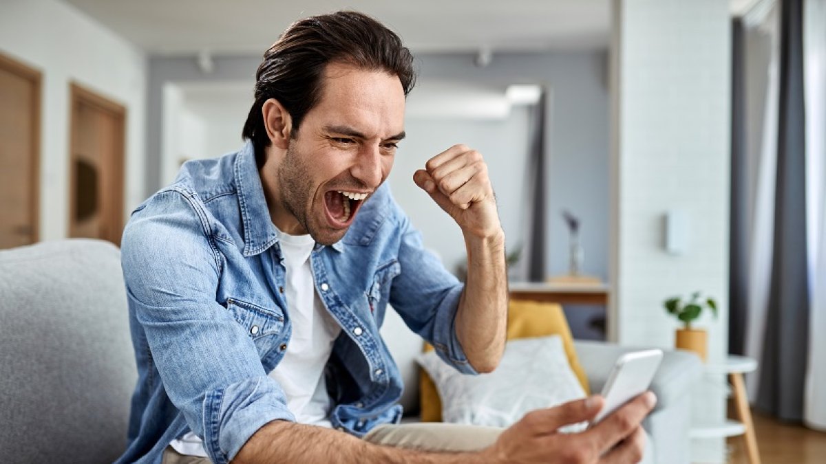 Happy man reading good news over smart phone and celebrating at home.