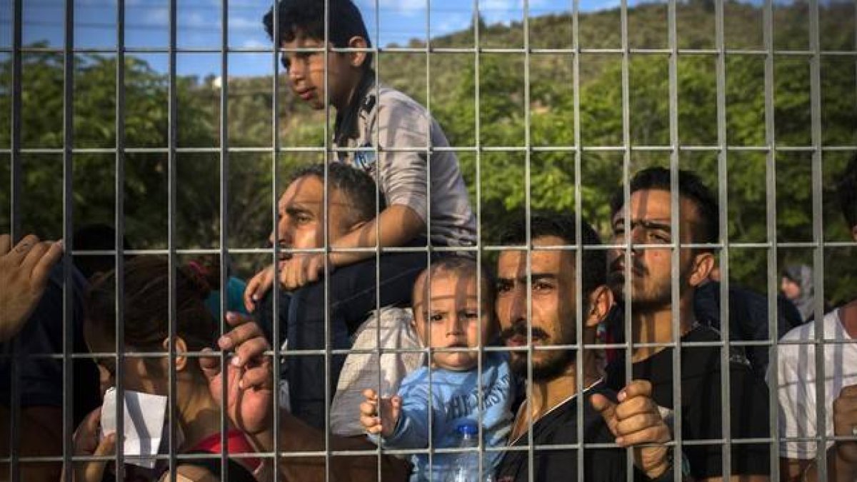 Refugiados e inmigrantes esperan tras una verja, en un campo de fútbol, a poder ser registrados, en Mitilene, este martes.-AP / SANTI PALACIOS