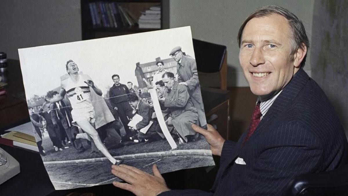 Roger Bannister, en una imagen de 1974, mostrando una foto de 20 años antes batiendo el récord de la milla.-AFP