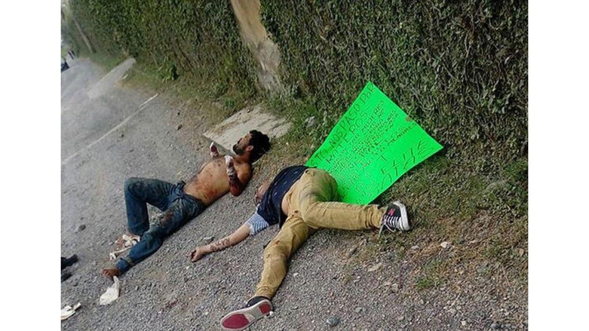 Dos de las víctimas en el suelo, junto a un cartel que les acusa de ladrones, firmado por un grupo de justicieros, este lunes en Guadalajara (México).-EFE