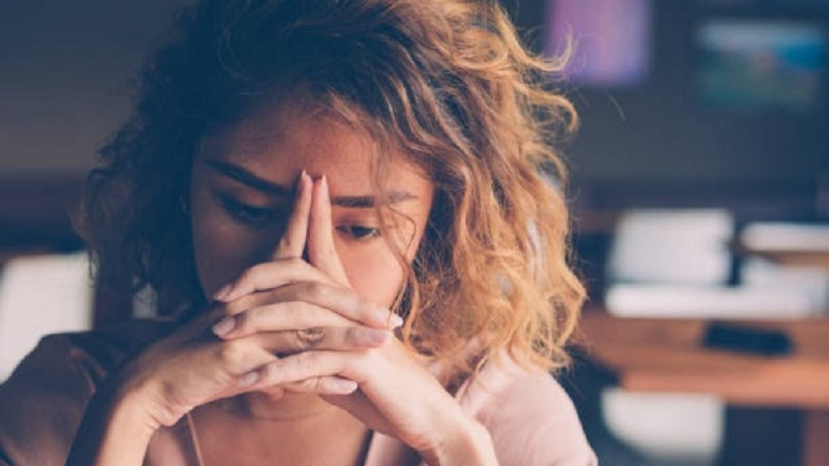 Closeup of sad young Asian woman at cafe leaning head on clasped hands and staring into vacancy. Tired freelancer feeling burnout. Stress and bad news concept