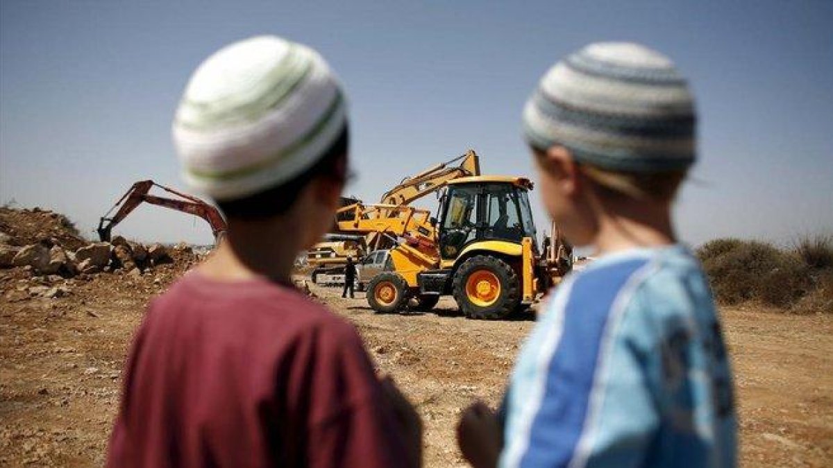 Dos niños judíos observan una retroexcavadora utilizada en la construcción de unas 50 viviendas en el asentamiento judío de Ariel .-EFE / OLIVIER WEIKEN