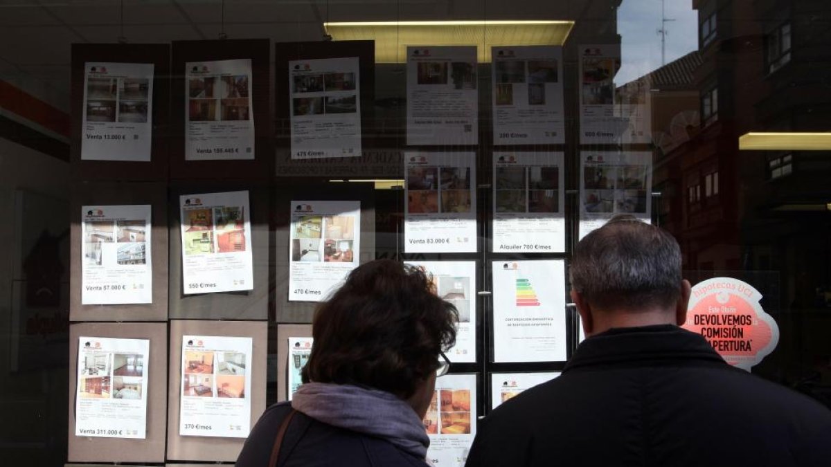 Una pareja mira los anuncios de venta de pisos en una inmobiliaria.