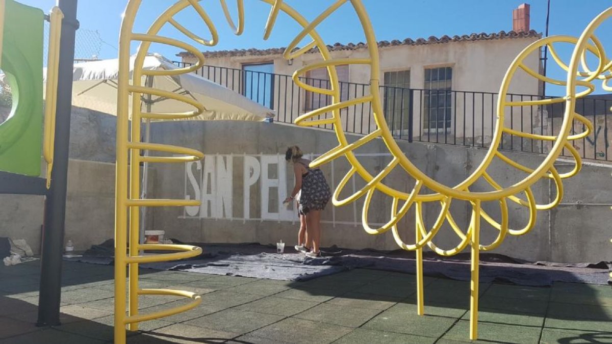 La encargada de coordinar el mural comienza a perfilar el dibujo con el nombre del pueblo.-EL MUNDO