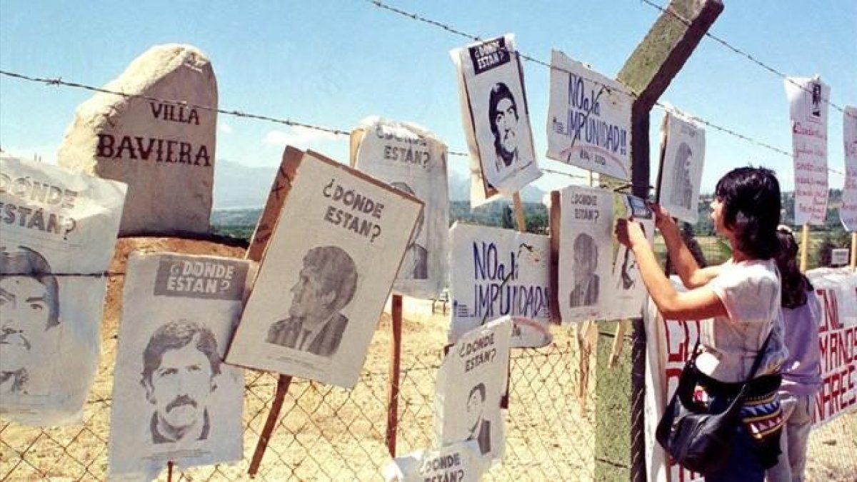 Una mujer cuelga carteles de chilenos desaparecidos en la cerca de Colonia Dignidad, que sirvió de centro de tortura de Pinochet.-REUTERS