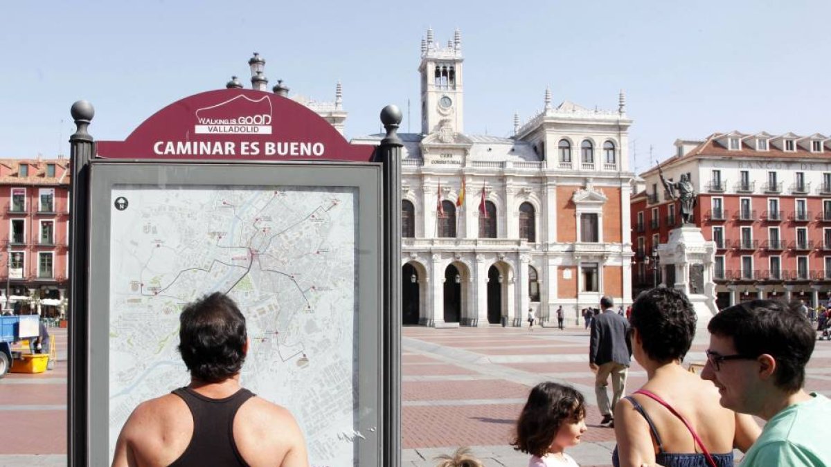 Una familia de turistas observa el panel informativo de las rutas 'Caminar es bueno' en la Plaza Mayor de Valladolid-Ical