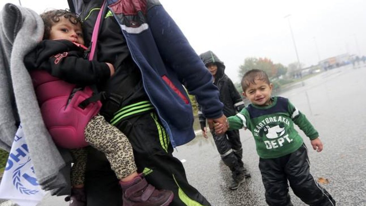 Un hombre camina llevando a dos niños bajo la lluvia junto a la frontera con Eslovenia.-SRDJAN ZIVULOVIC / REUTERS