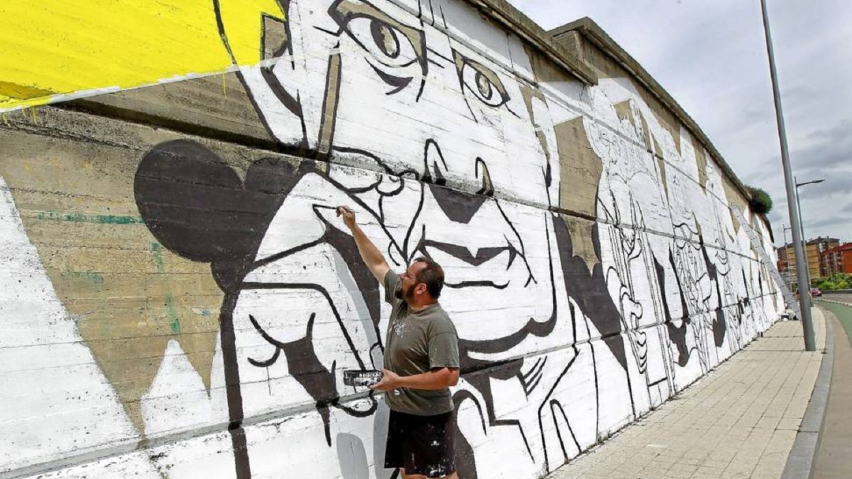 Un artista pinta la cara de Miguel Delibes en el mural de la Avenida Salamanca, en dirección al Puente de la Hispanidad-J. M. Lostau