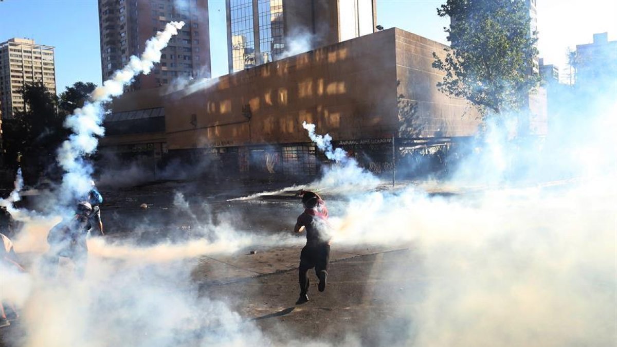 Un grupo de personas se enfrenta a la policía antidisturbios, este viernes, en la Plaza Italia en Santiago de Chile durante una nueva jornada de protestas en contra del gobierno del presidente Sebastián Piñera.-EFE / ELVIS GONZÁLEZ