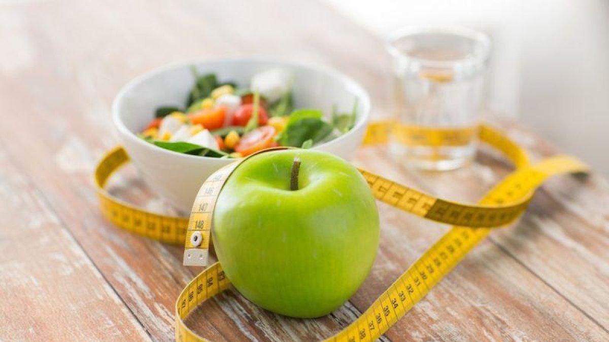 Manzana, cinta métrica y desayuno en una mesa.-123RF