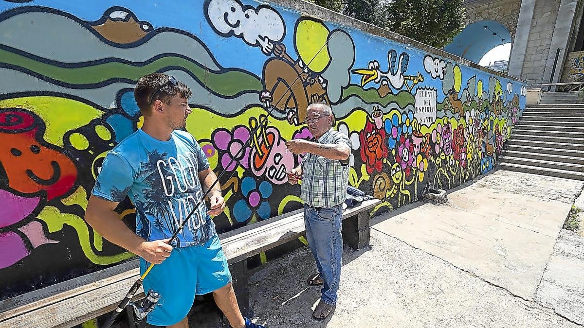 Dos pescadores delante de uno de los murales de los alrededores de la Playa de Las Moreras.-PHOTOGENIC / PABLO REQUEJO