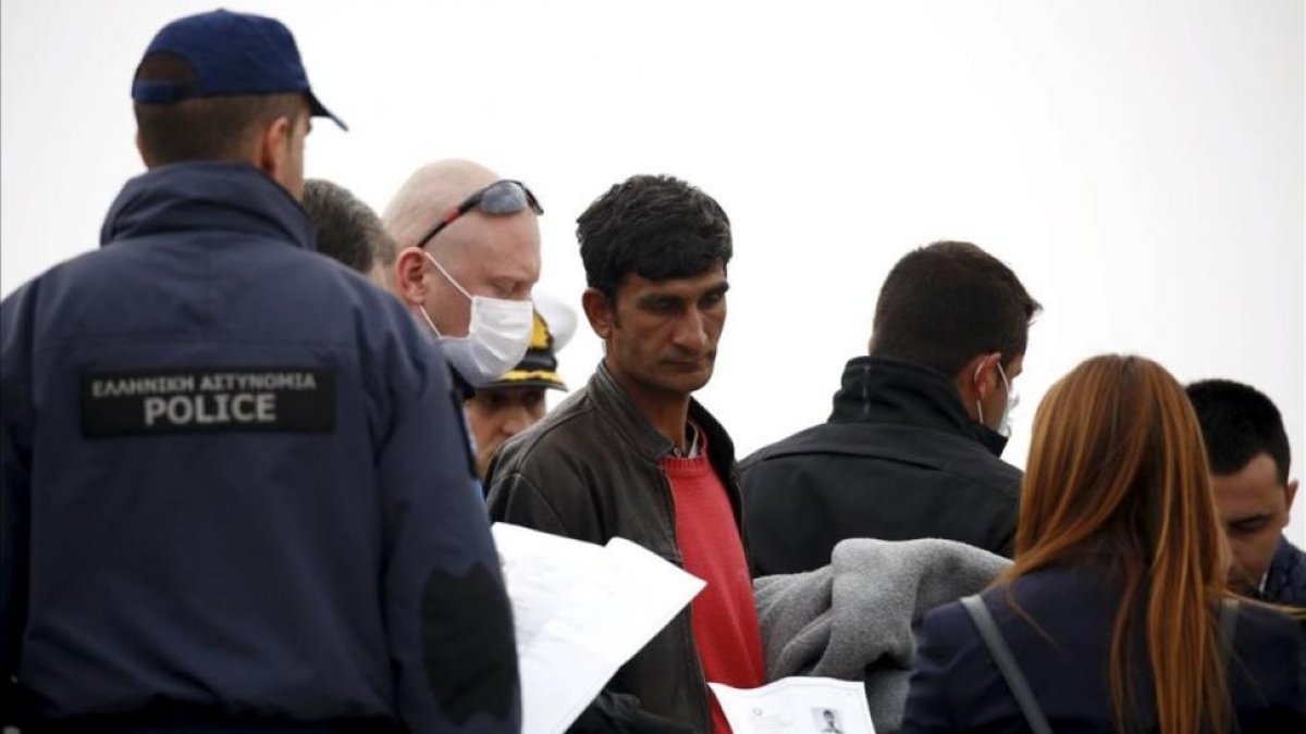 Un funcionario de la UE sostiene la documentación de un migrante (centro) en un barco que les traslada de regreso a Turquía desde Lesbos, este viernes.-REUTERS / GIORGOS MOUTAFIS