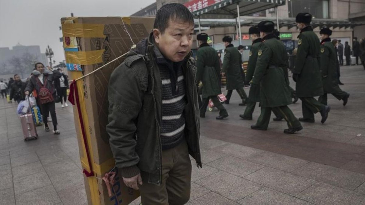 Un hombre llega con un gran televisor en la espalda a la estación central de Pekín, dispuesto a tomar un tren, el 26 de enero.-GETTY IMAGES / KEVIN FRAYER
