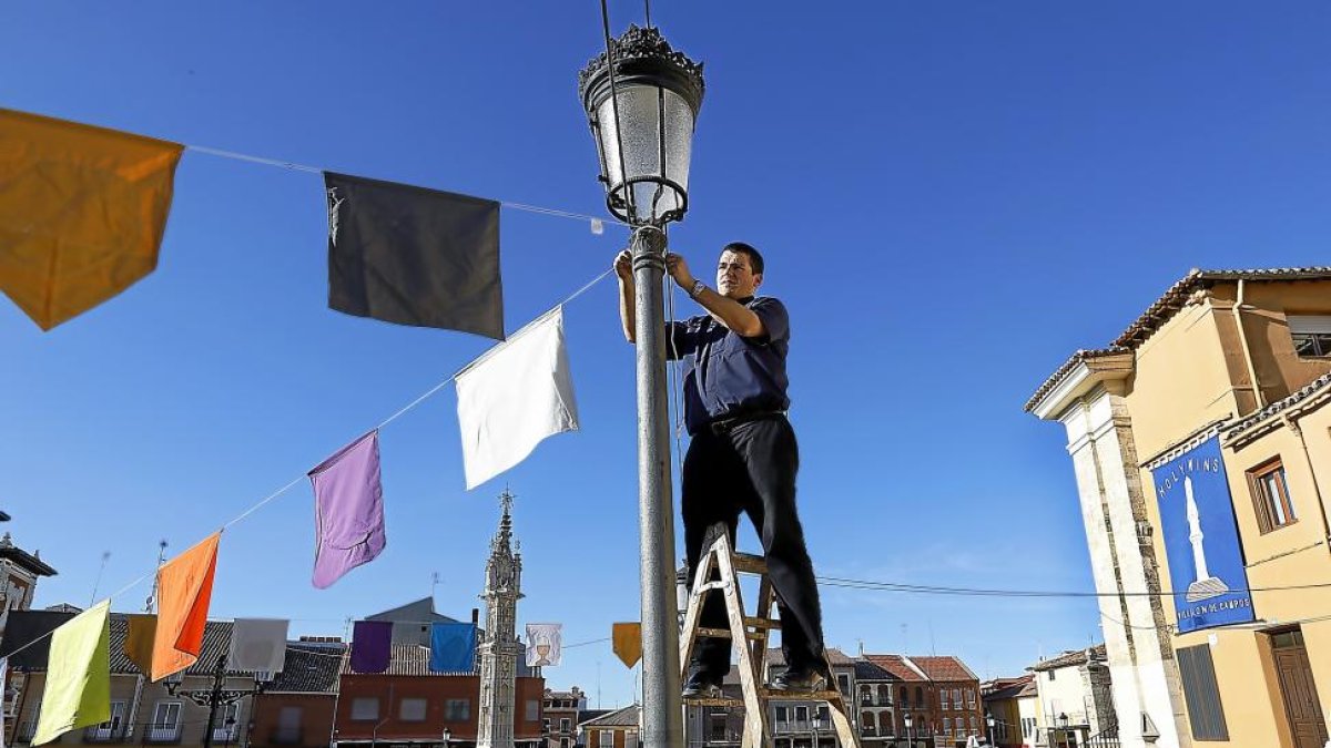 El párroco de Villalón, Francisco Casas, coloca los banderines en la plaza junto a El Rollo, tras haber instalado un gran cartel de ‘Holywins’.-J. M. LOSTAU