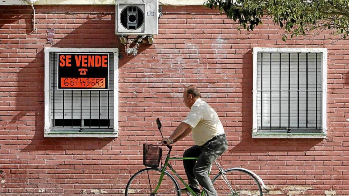 Un hombre en bicicleta pasa por delante de un cartel de 'Se vende' en una vivienda.-Carlos Márquez