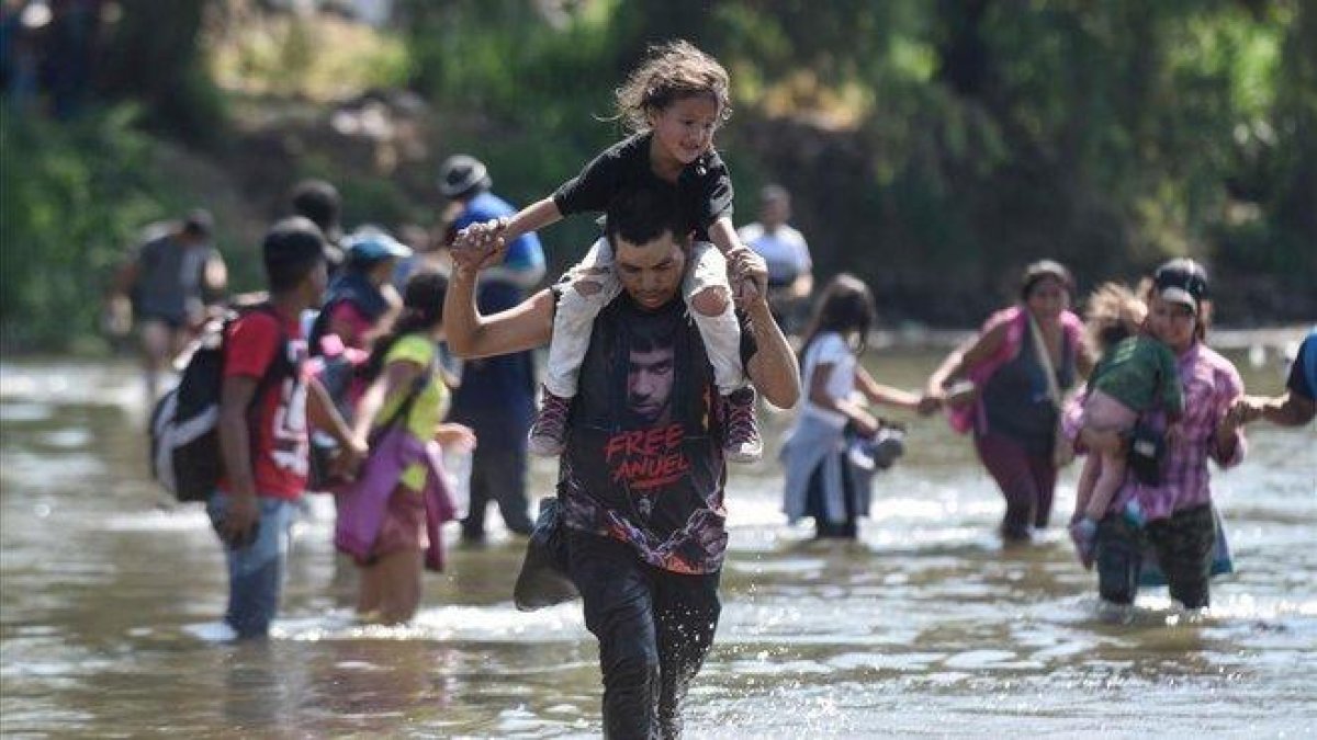 Varios migrantes cruzan el río Suchiate con sus hijos en brazos.-JOHAN ORDONEZ (AFP)