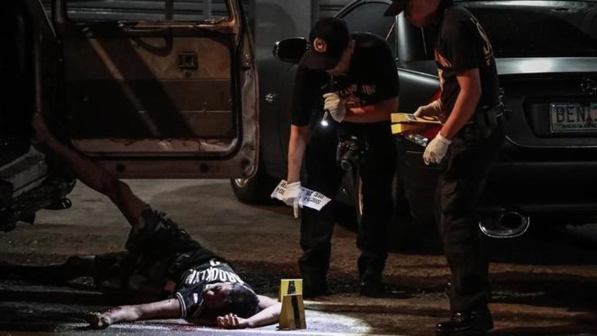 Un cadáver junto a un vehículo acribilladoen Manila.-EFE / EZRA ACAYAN