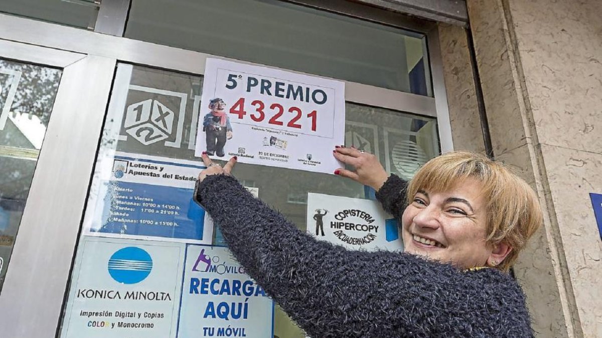 Carmen Lino pega el cartel del premio en su copistería del barrio de Pajarillos.-Miguel Ángel Santos