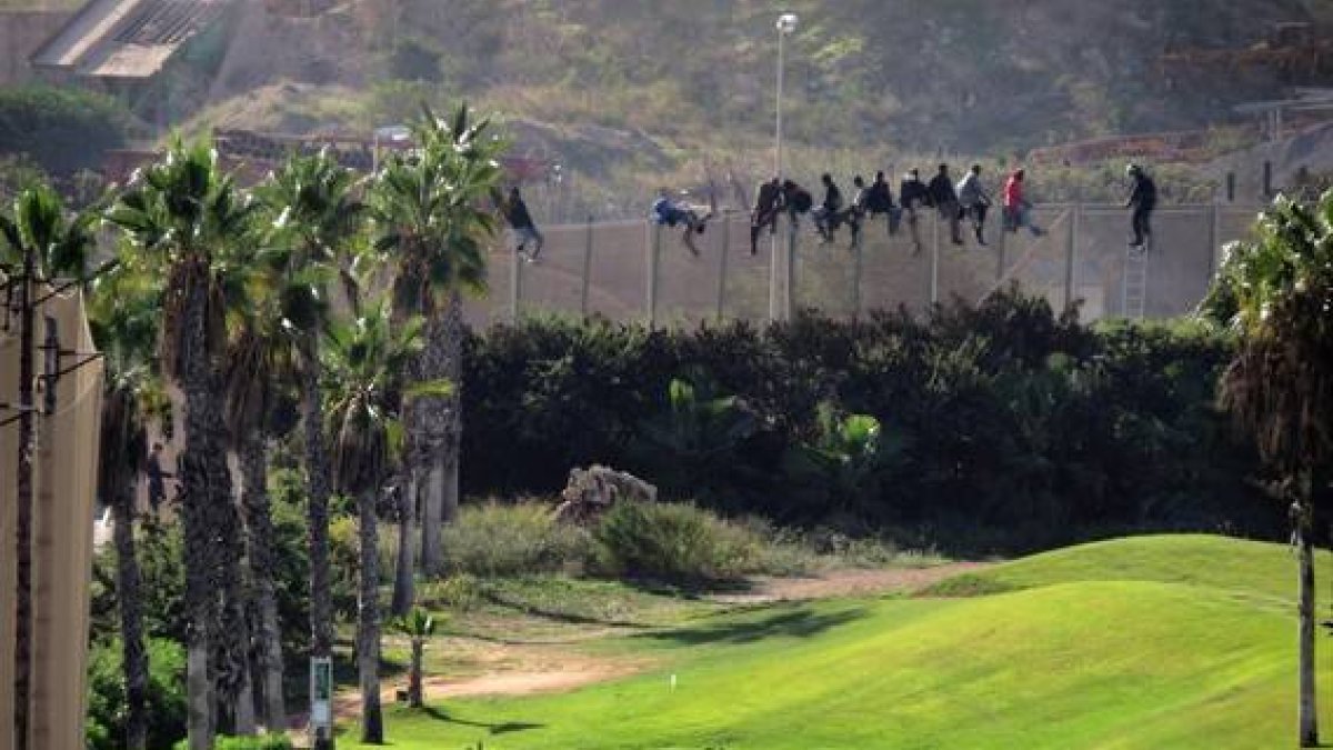 Inmigrantes encaramados en la valla de Melilla, el pasado octubre, mientras varias personas juegan en un campo de golf de la ciudad autónoma.-Foto: AP/ Jose Palazon