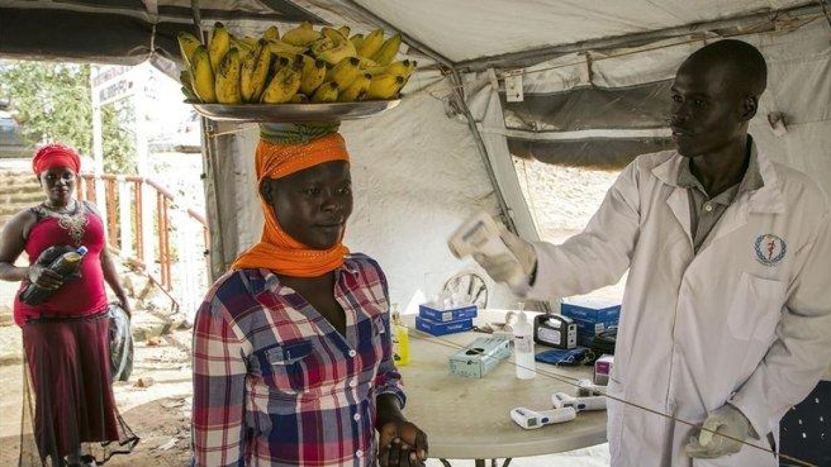 Un trabajador sanitario comprueba el estado de varias personas en la frontera de Nimule, en Uganda.-AFP / AKUOT CHOL