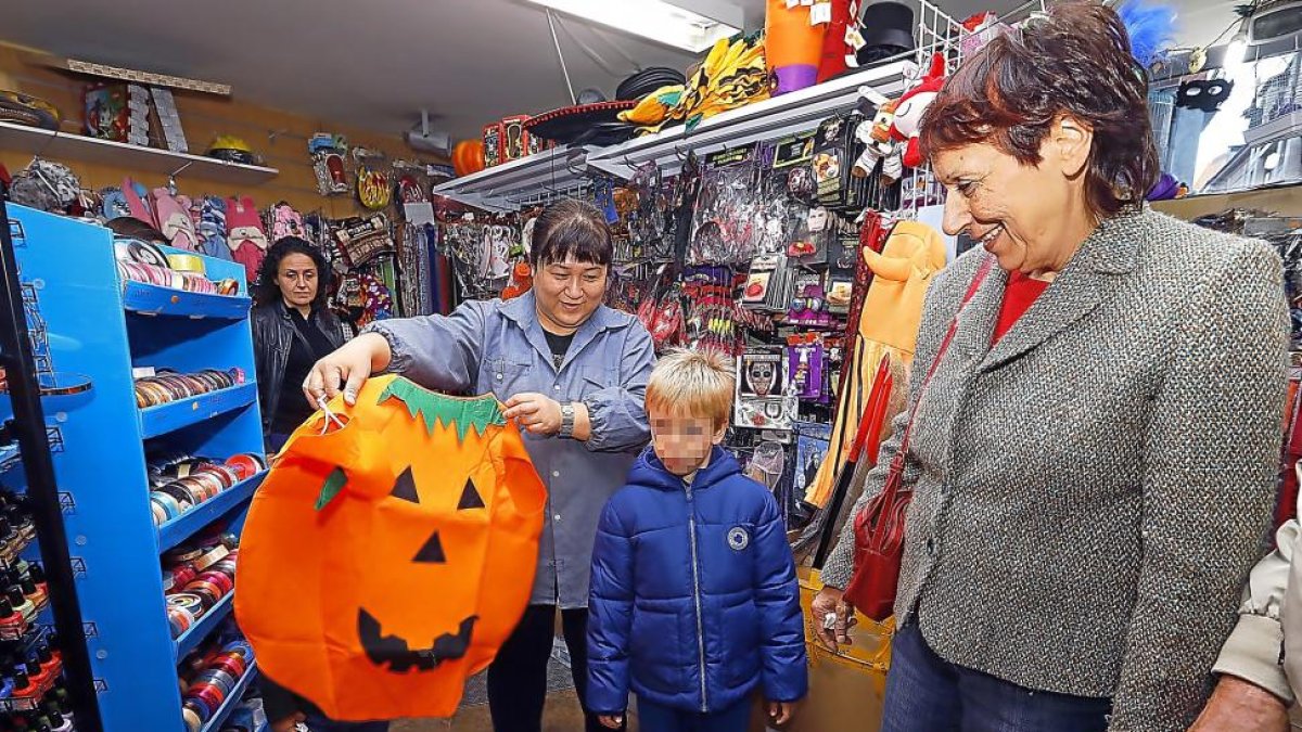 La dependienta de un bazar muestra un disfraz de calabaza  a un niño y su abuela.-J.M. LOSTAU