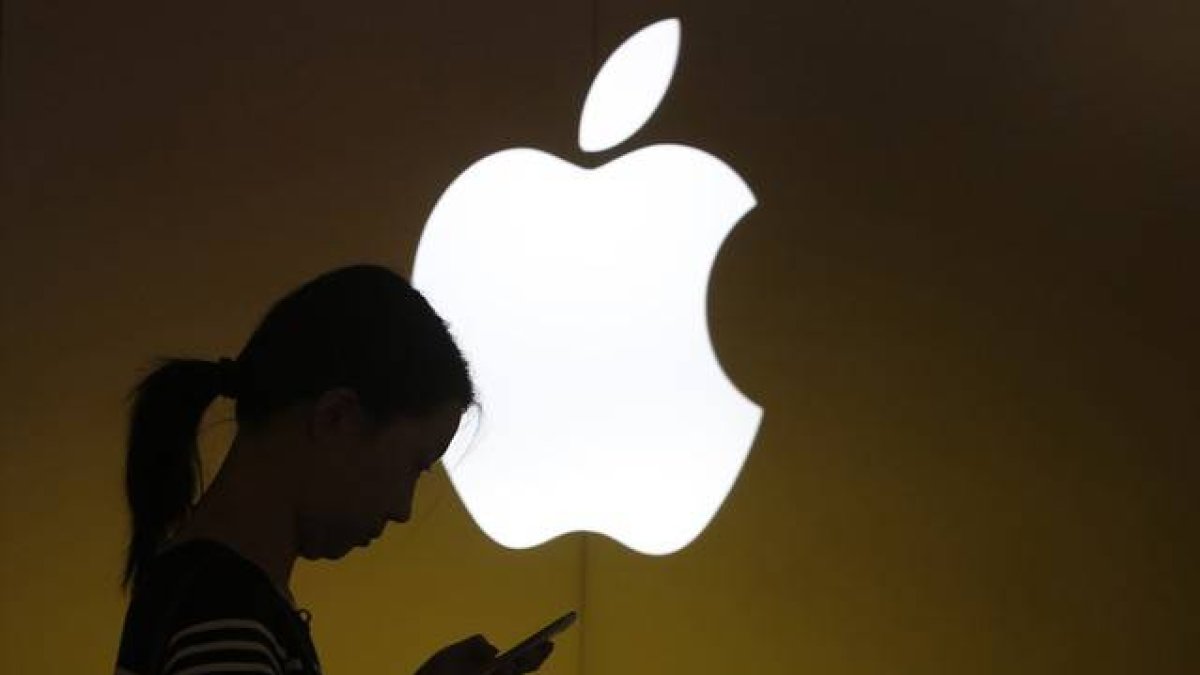 Una mujer mira su teléfono ante el logo de Apple en la tienda oficial de Shangai, China.-Foto: REUTERS / ALY SONG