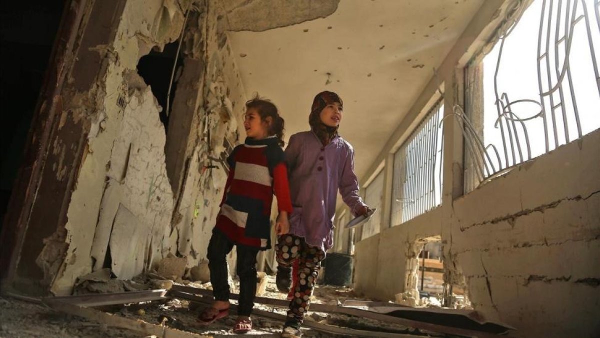 Dos niñas sirias recorren su escuela, destrozada el día anterior por los ataques áereos de la aviación gubernamental, en la sitiada ciudad de Saqba (Guta Oriental), el 9 de noviembre.-/ AFP / AMER ALMOHIBANY