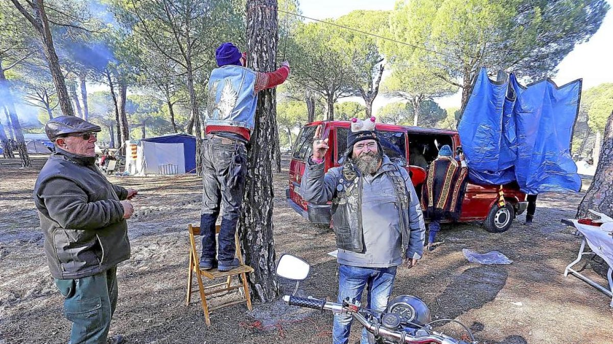 Un motero veterano saluda en su ‘campamento’ del Pinar de Valdegalindo, mientras su amigo cuelga un toldo.-ICAL