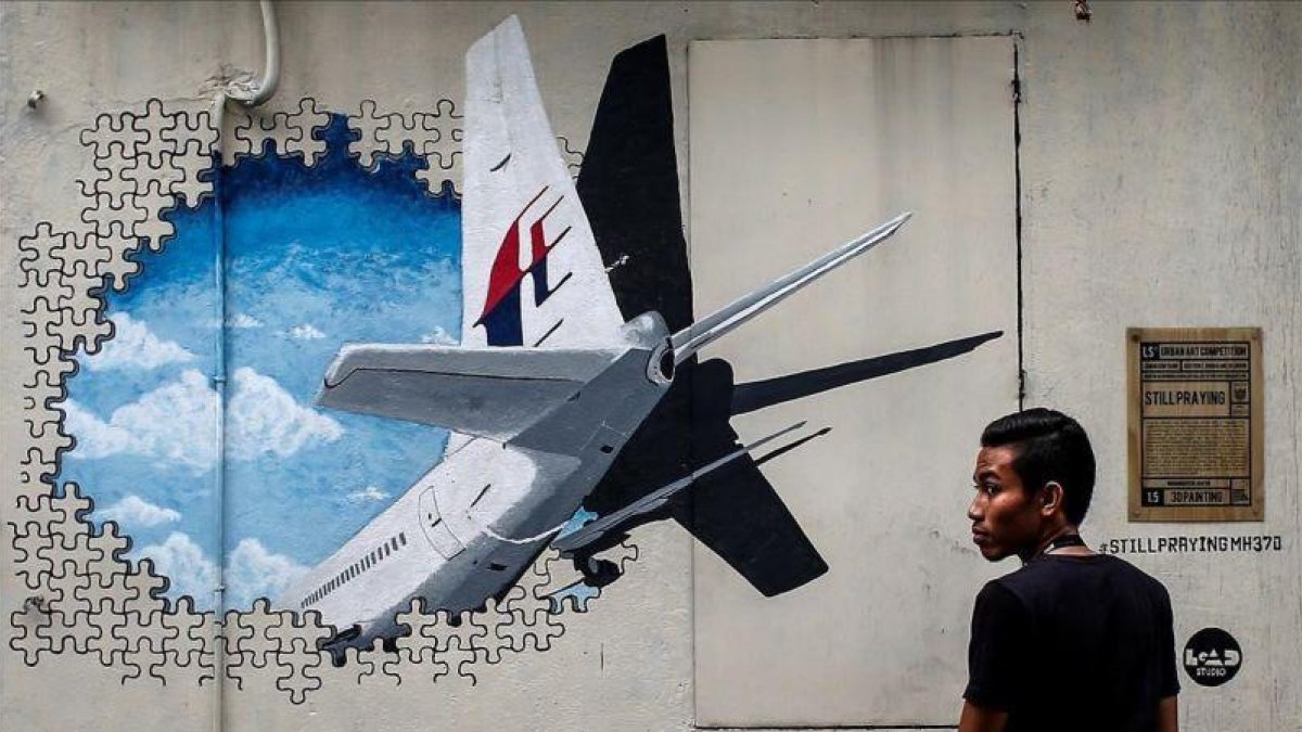 Un joven pasa por delante de un  mural del vuelo MH370 de Malaysia Airlines en Kuala Lumpur el 6 de marzo del 2015.-FAZRY ISMAIL (EFE)