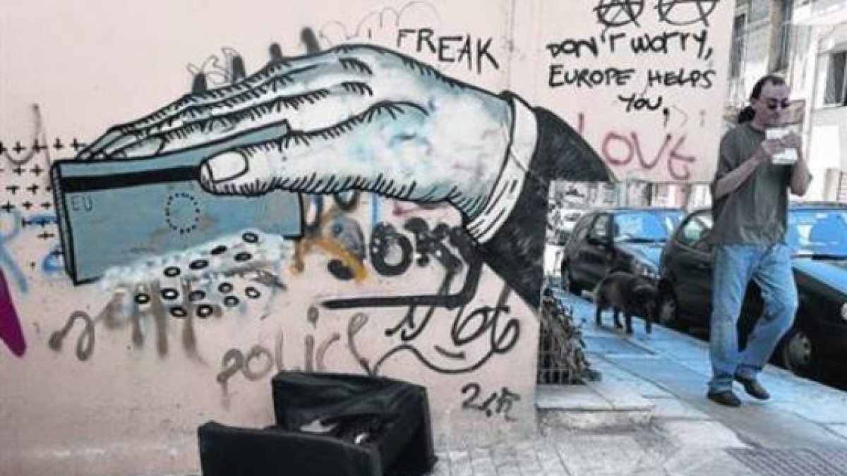 Un hombre pasa ante un grafiti de denuncia en la ciudad de Atenas, este lunes.-Foto: EL PERIÓDICO