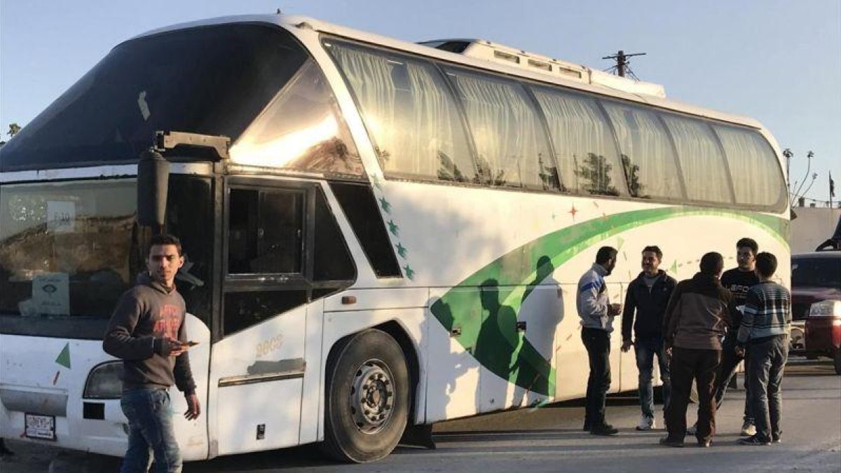 Varias personas permanecen junto a un autobús a la espera de la llegada del resto de evacuados civiles y combatientes.-EFE / MOHAMED BADRA