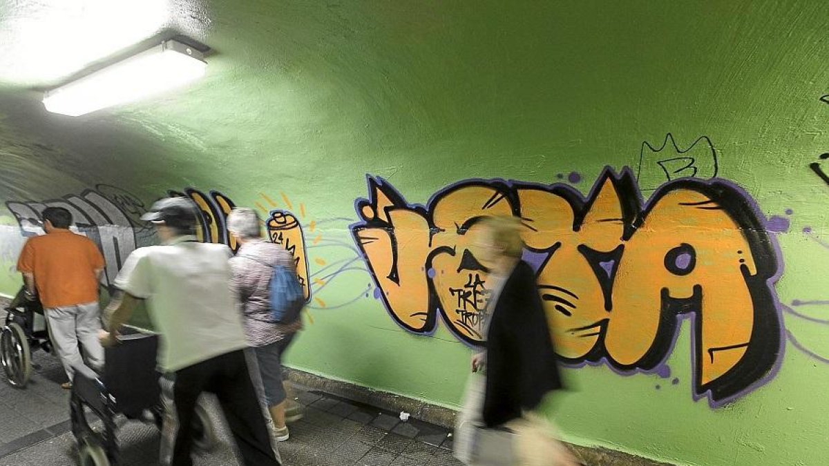 Un grupo de personas pasa  ante un apintada en un pasadizo subterráneo.-E. M.