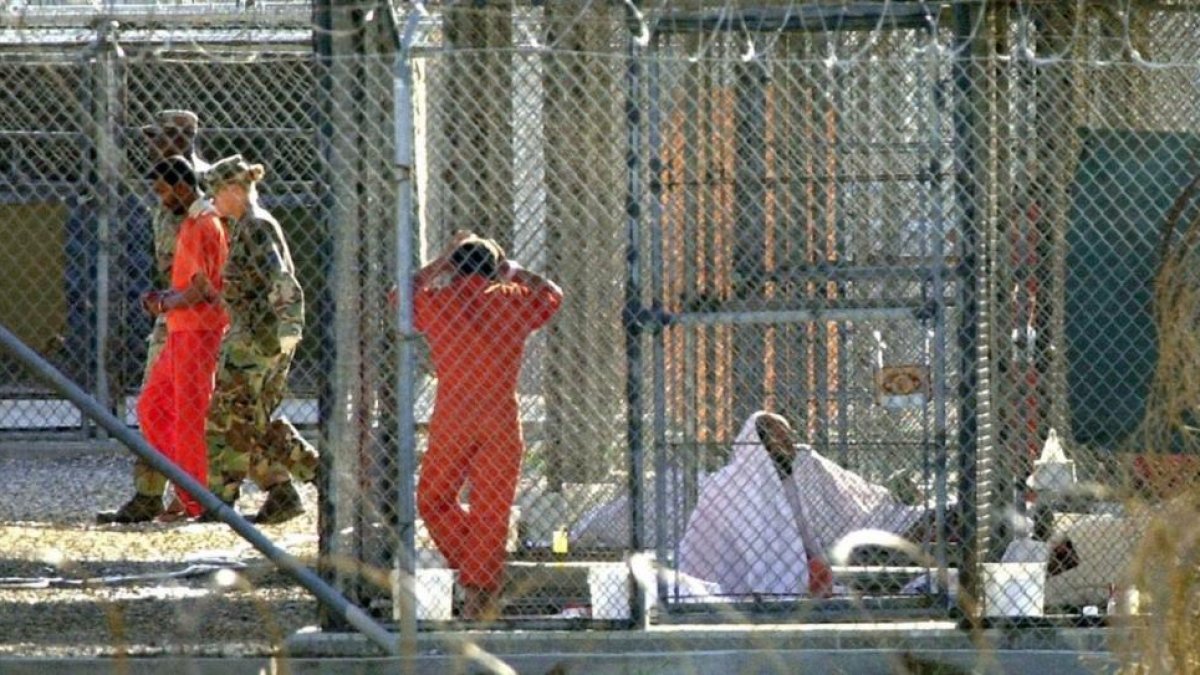 Un recluso de Guantánamo, escoltado por dos guardias en el penal, junto a otros dos presos en sus celdas, el 15 de marzo del 2002.-AP / TOMAS VAN HOUTRYVE