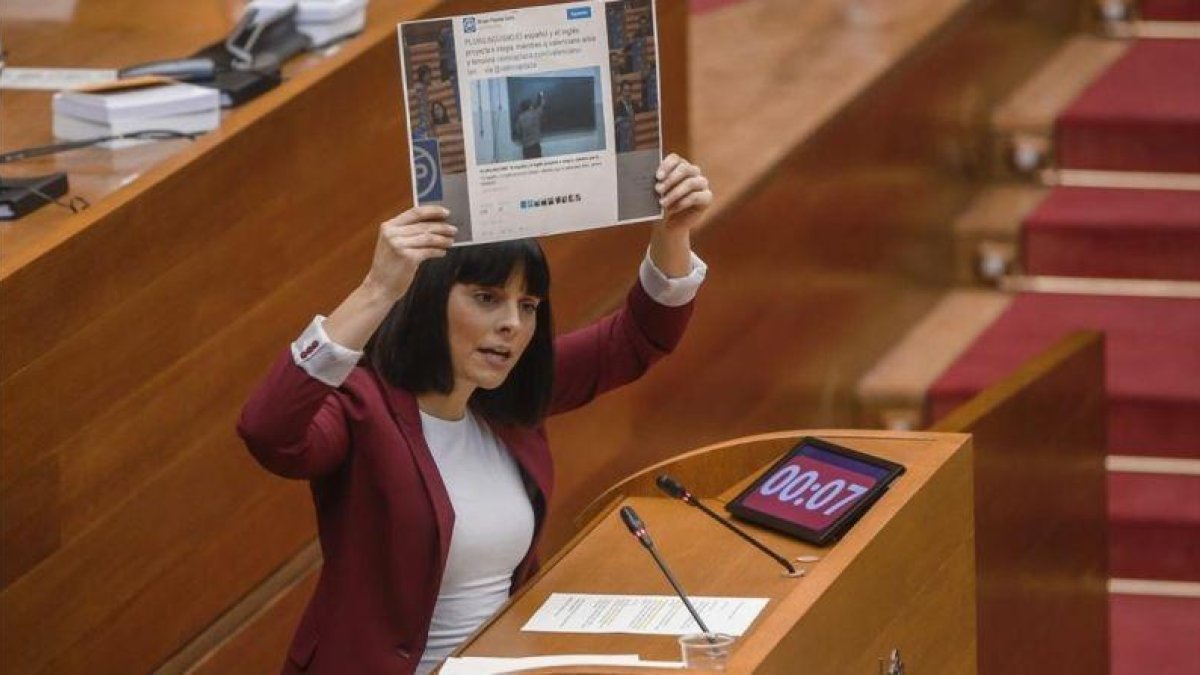 Sandra Miguez muestra, en el pleno de las Corts, un tuit del grupo popular en el que se hace eco del titular de una entrevista a un profesor, criticado por la diputada de Podemos durante su intervención.-MIGUEL LORENZO