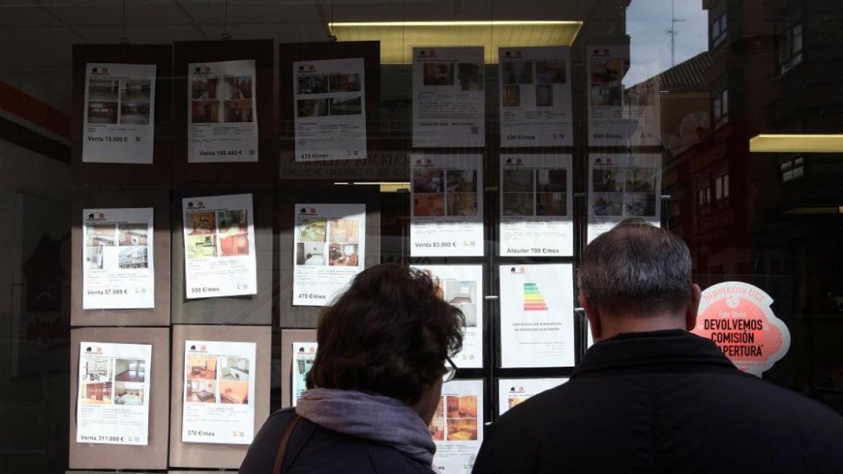 Una pareja mira precios de pisos en una inmobiliaria.-ICAL