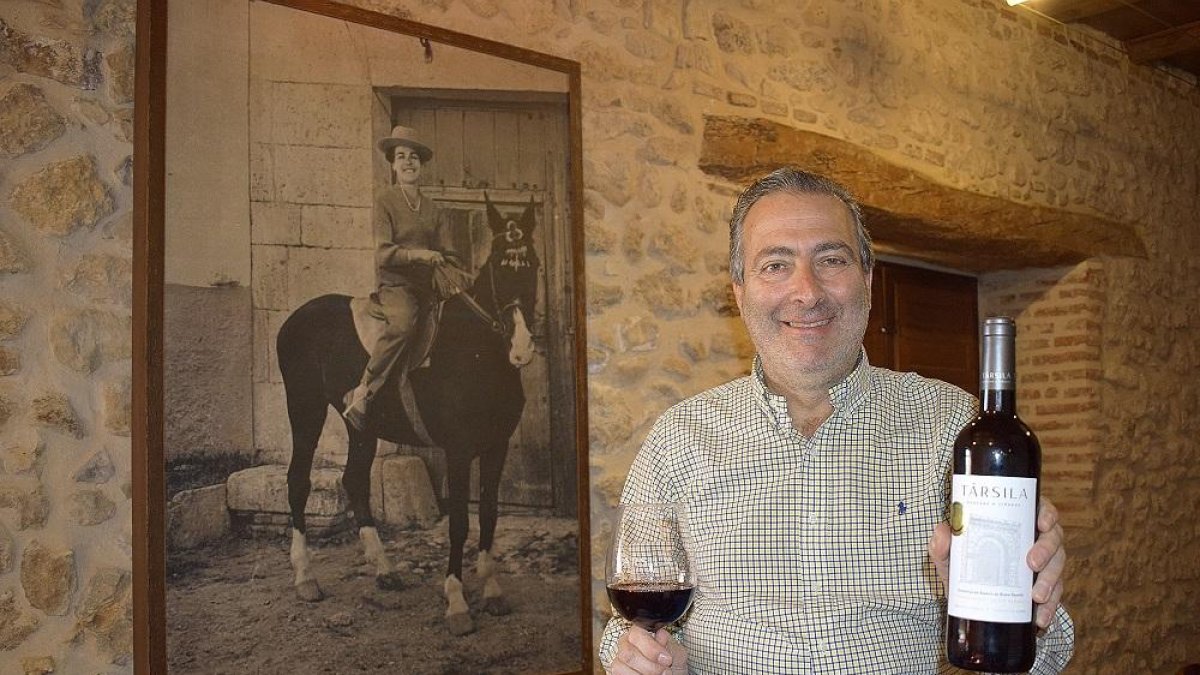 Ricardo Rodilla enseña una botella en el interior de la bodega tradicional ante la mirada de una foto de su madre, Társila a caballo.-ARGICOMUNICACIÓN