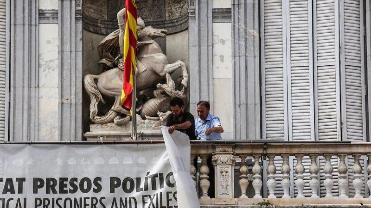 Dos trabajadores de la Generalitat retiran la pancarta que colgaba del Palau.-ÁNGEL GARCÍA