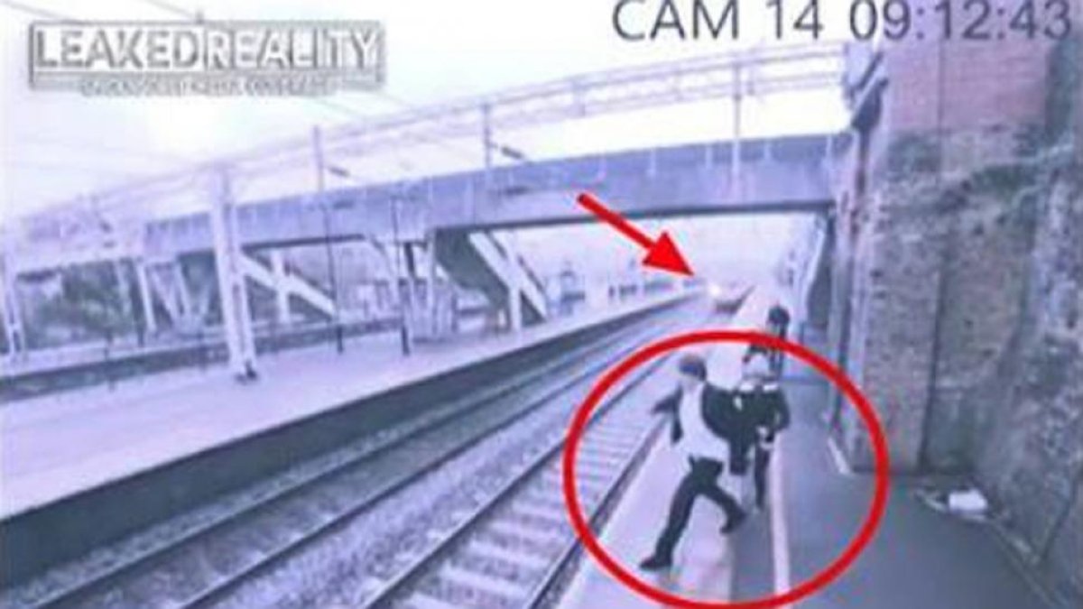 Momento en el que la mujer, detrás del hombre, le agarra del brazo y evita que se tire a la vía de tren.-/ LIVE LEAK / CCTV