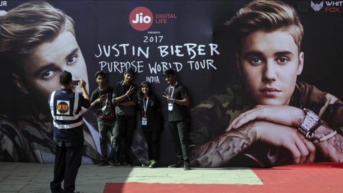 Varios jovenes indios se toman una fotografia con un cartel que publicita la gira mundial del cantante canadiense Justin Bieber antes de su concierto en el estadio Dnyandeo Yashwantrao Patil  en Bombay (India).-EFE / DIVYAKANT SOLANKI
