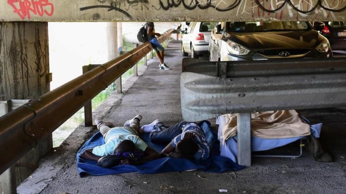 Unos inmigrantes tratan de descansar en el párking ubicado bajo un puente en la localidad italiana de Ventimiglia.-MIGUEL MEDINA (AFP)