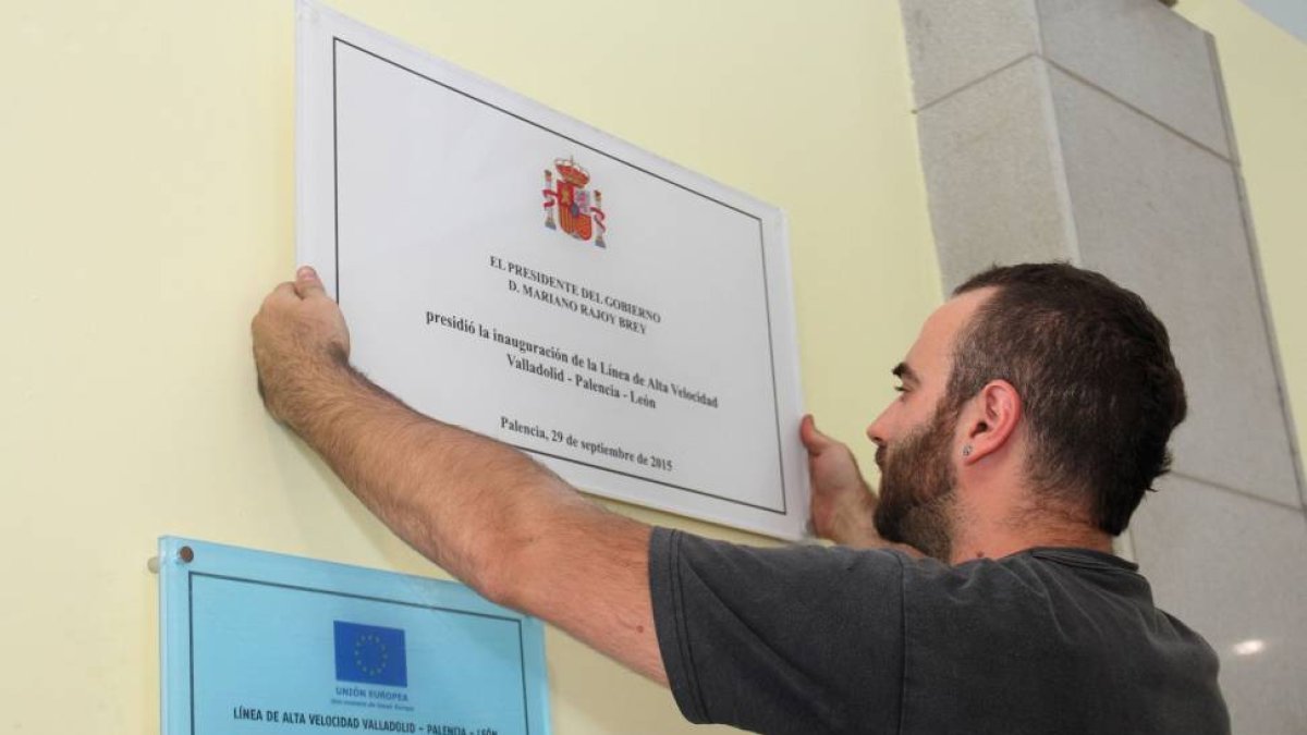 Un operario coloca la placa conmemorativa de la inauguración de la línea de Alta Velocidad en la estación de Palencia, con el nombre de Palencia corregido.-ICAL