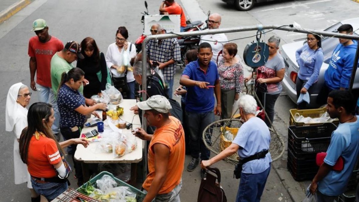 Venezolanos hacen cola para pagar la fruta y las verduras en un mercado callejero, en Caracas, el 13 de noviembre.-REUTERS / MARCO BELLO