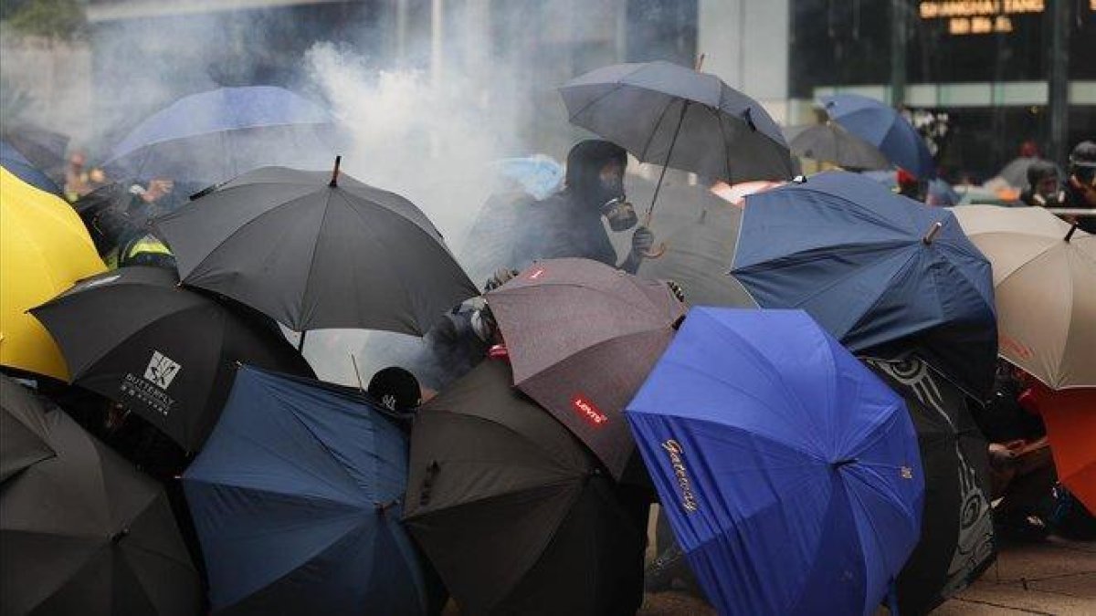 Varios manifestantes se protegen con paraguas de los gases lacrimógenos lanzados por la policía, este domingo en Hong Kong.-AP /  / VINCENT THIAN